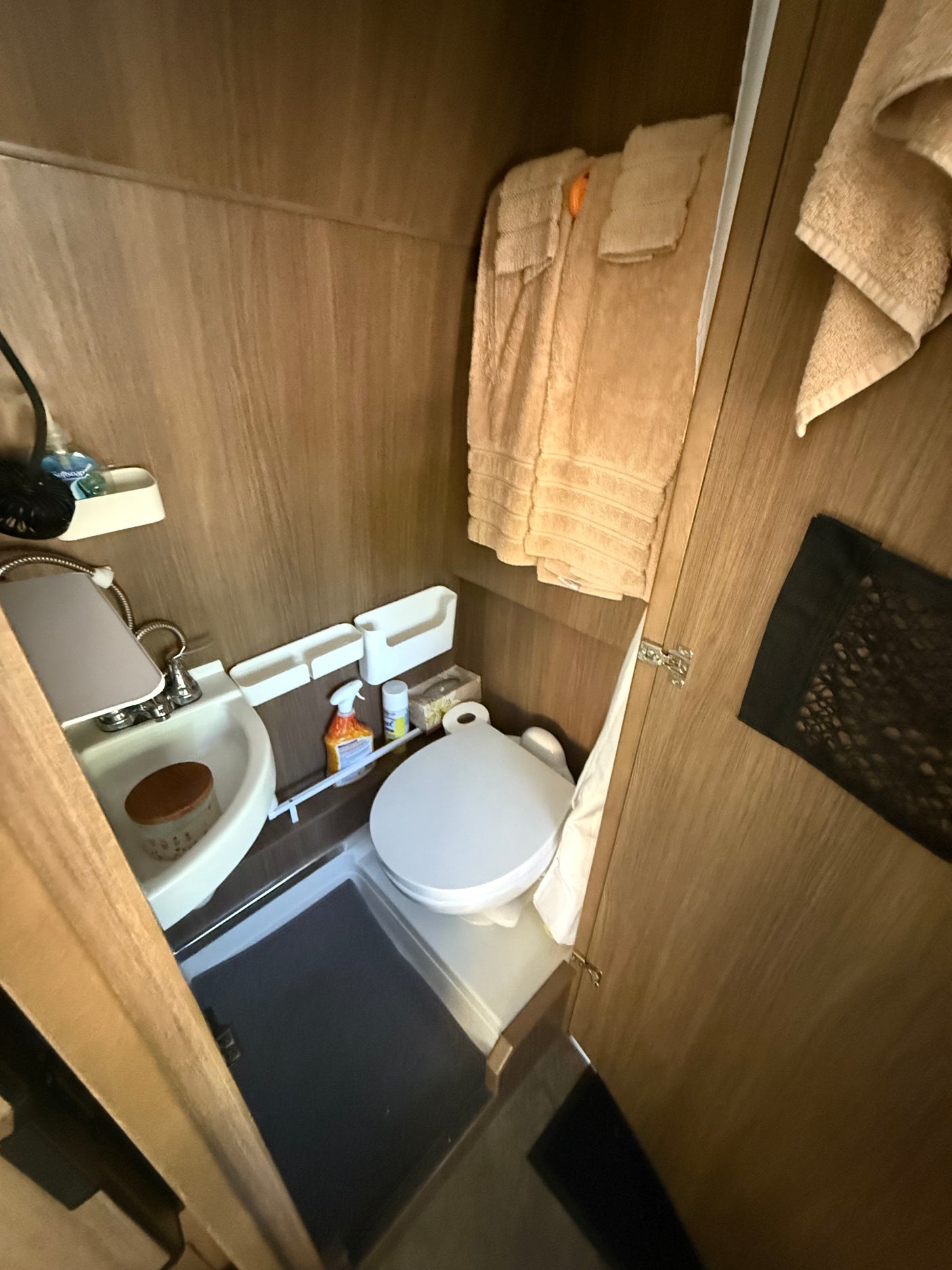 RV rental bathroom with a white toilet, corner sink, storage, and light brown towels.