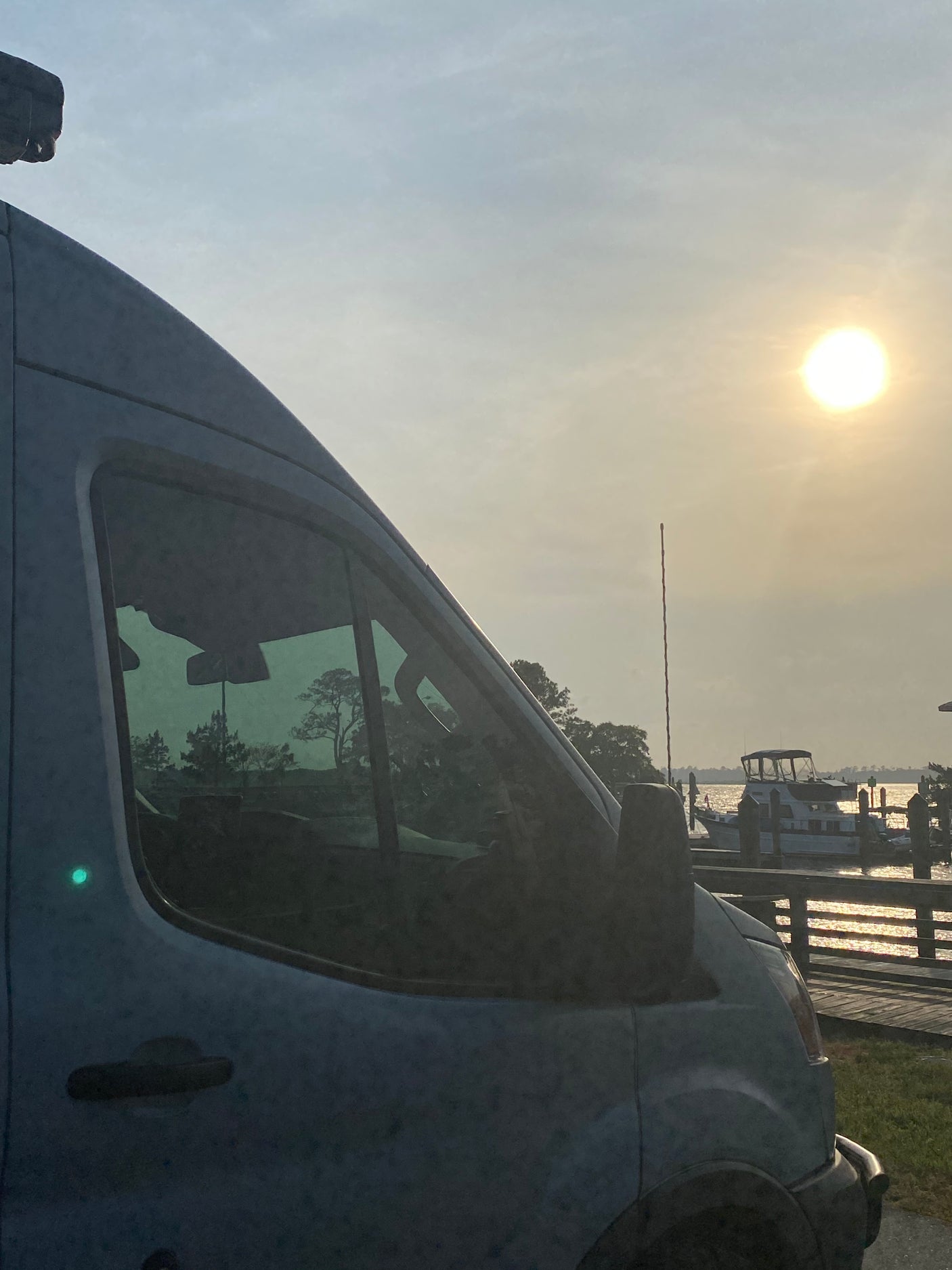 RV rental camper van at a tranquil marina. Bright sunset illuminates boats on the water and trees in the distance.