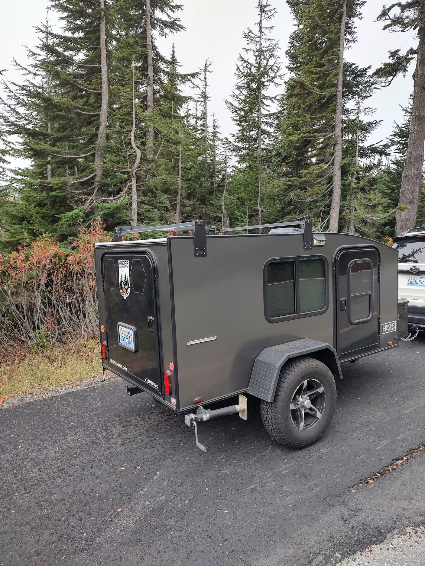 An RV rental, this Hiker Teardrop Trailer with off-road tires is parked in a forest of tall pines, perfect for camping.