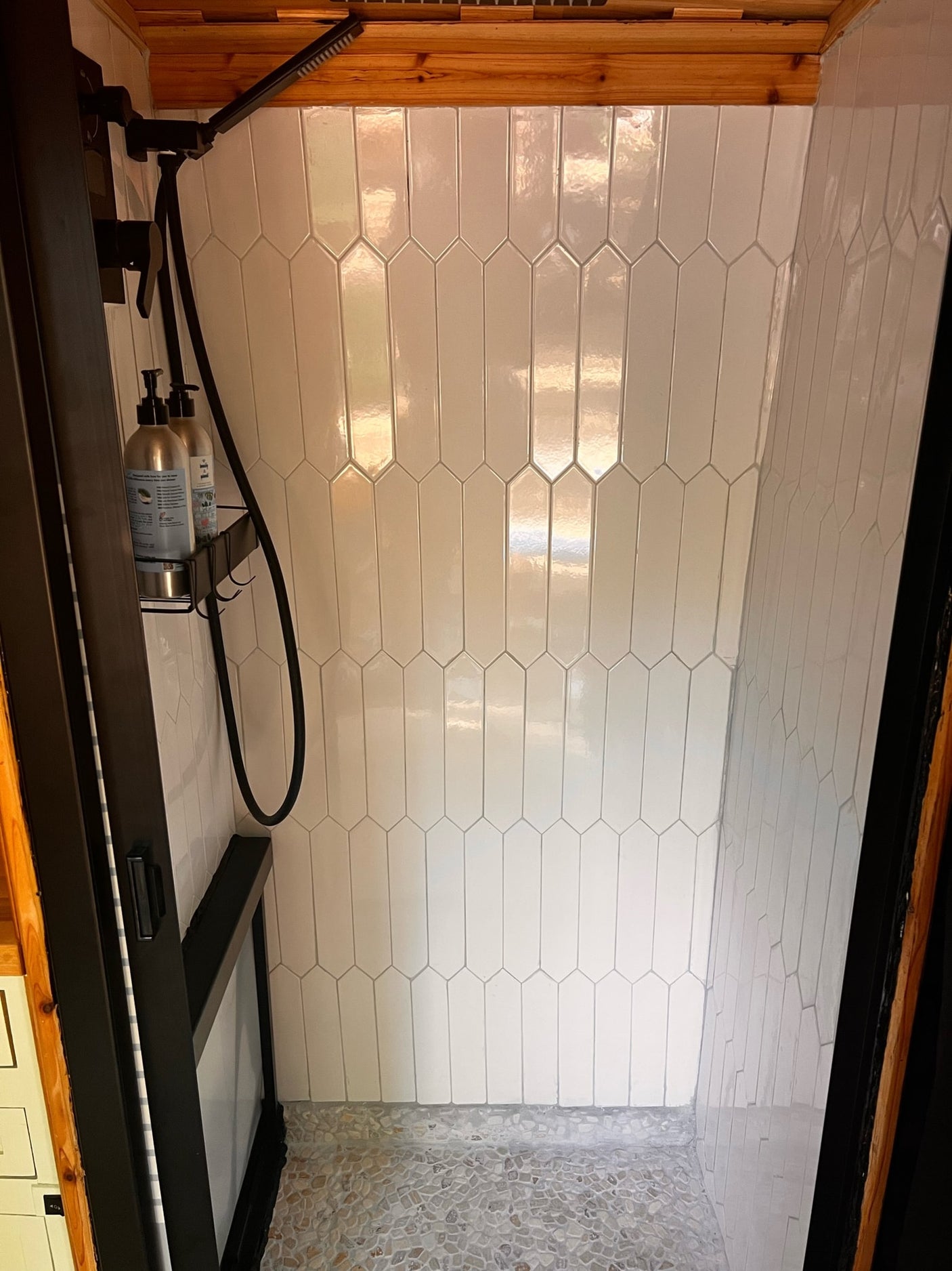 Modern RV rental shower featuring white picket tiles, pebble floor, and sleek black fixtures. Ideal for travel.