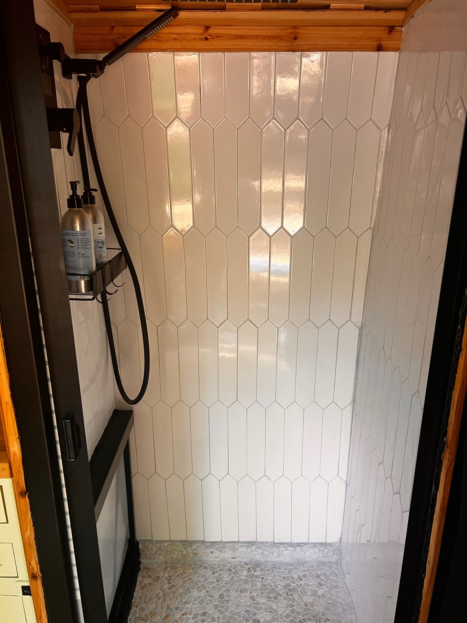 Modern RV rental shower featuring white picket tiles, pebble floor, and sleek black fixtures. Ideal for travel.
