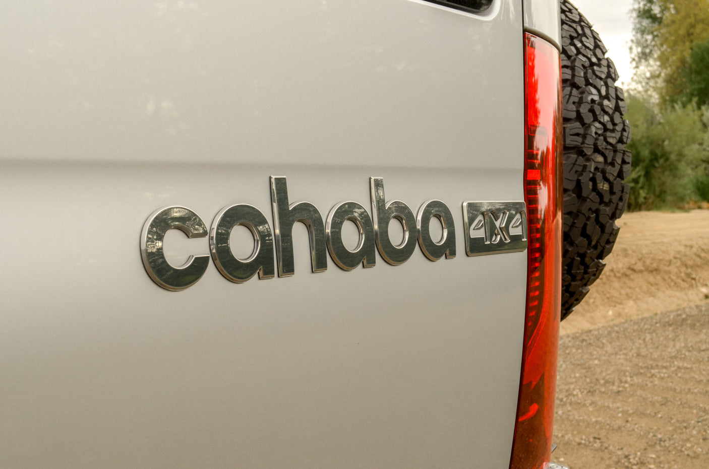 Rear view of a Cahaba 4x4 RV rental, highlighting its rugged tire, red taillight, and distinctive emblem.