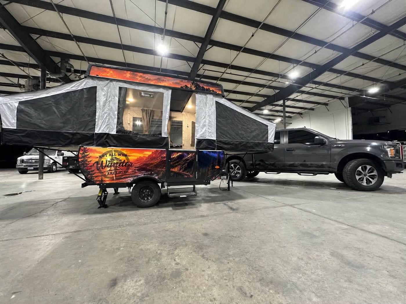is parked for adventure at a sunny campsite.|This RV rental pop-up camper features vibrant mountain art & "Not All Who Wander Are Lost" text — photo 3