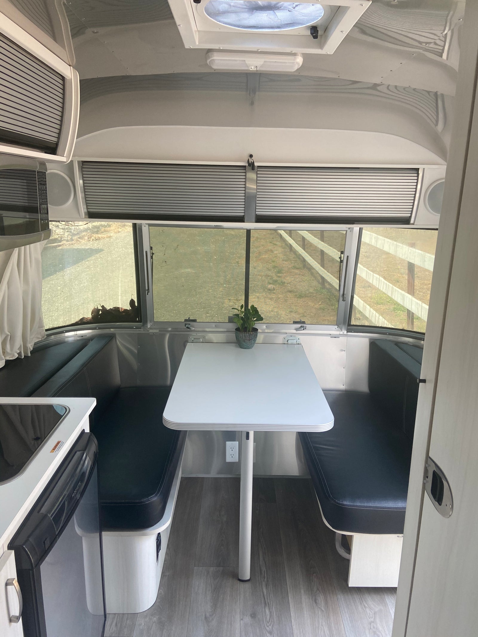 Modern RV rental interior: A bright dinette with black benches, overhead storage, and kitchen area for comfortable travel.
