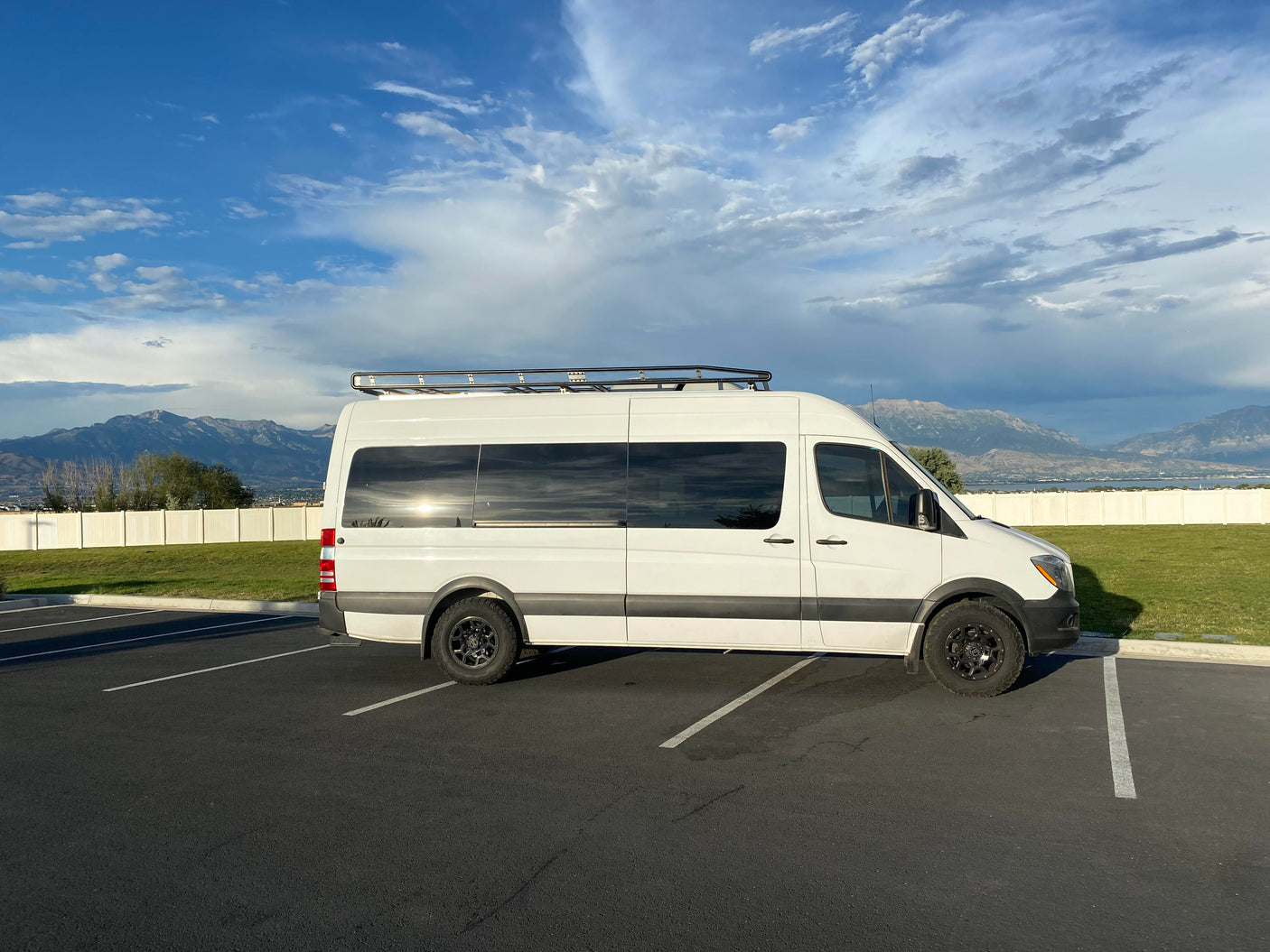 Explore with this white RV rental van, parked amidst mountains and a lake under a beautiful, cloudy sky.