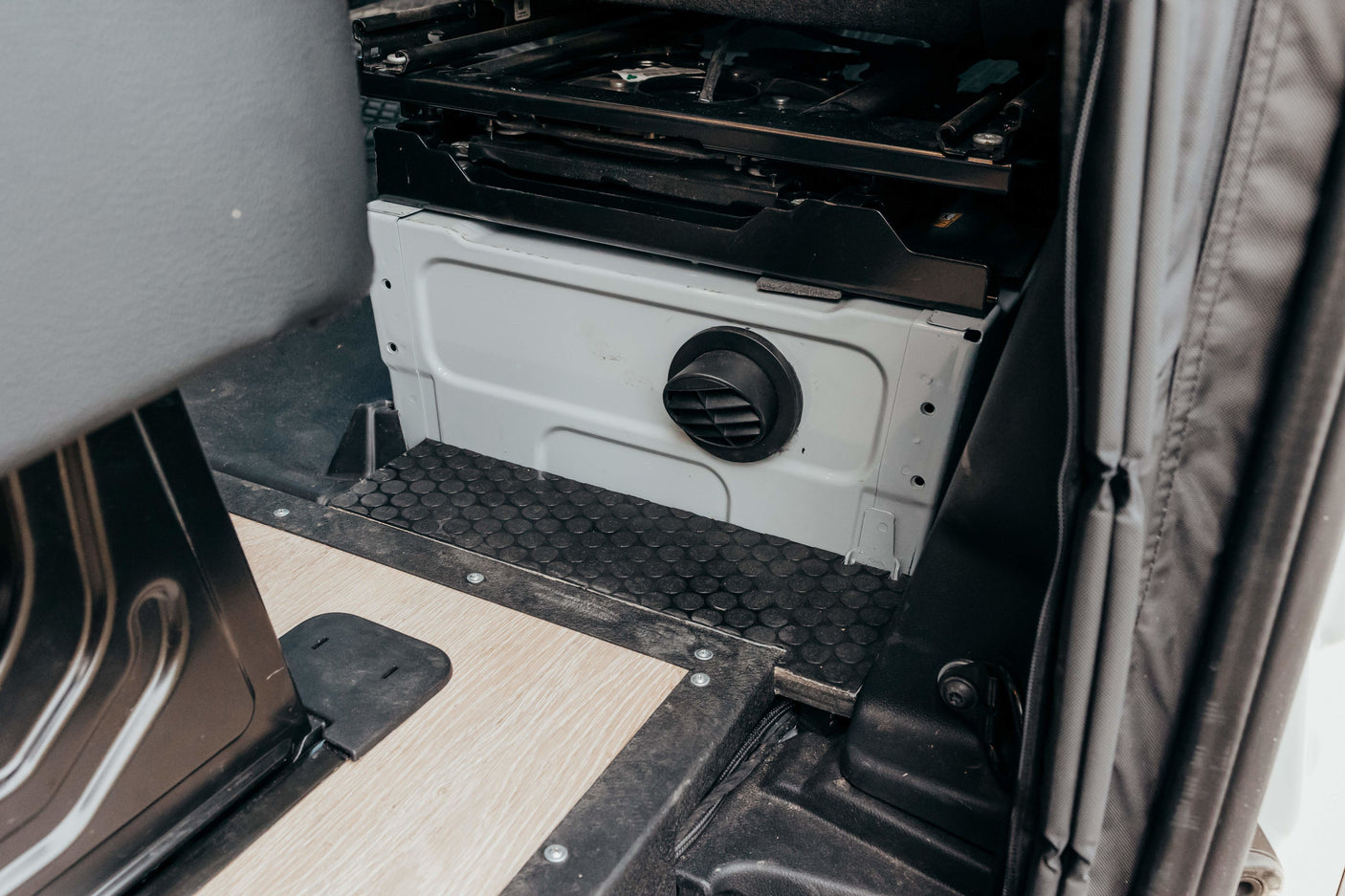 RV rental: Camper van interior with passenger swivel seat base, circular air vent, and custom flooring.