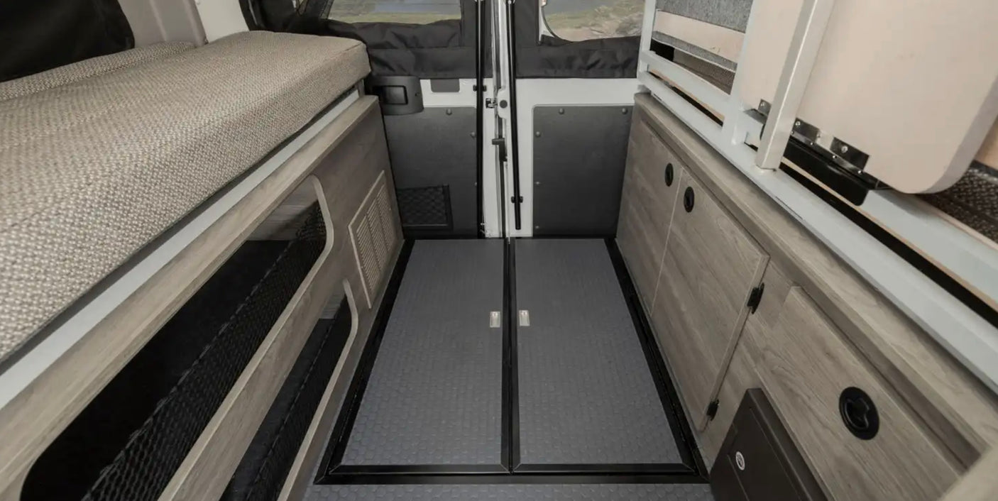 Compact RV rental interior featuring a bed, ample storage cabinets, and durable textured flooring. Ideal for road trips.