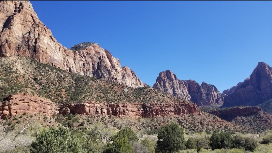 Towering red cliffs and green valleys under a blue sky. Discover this majestic national park with an RV rental for an unforgettable adventure.