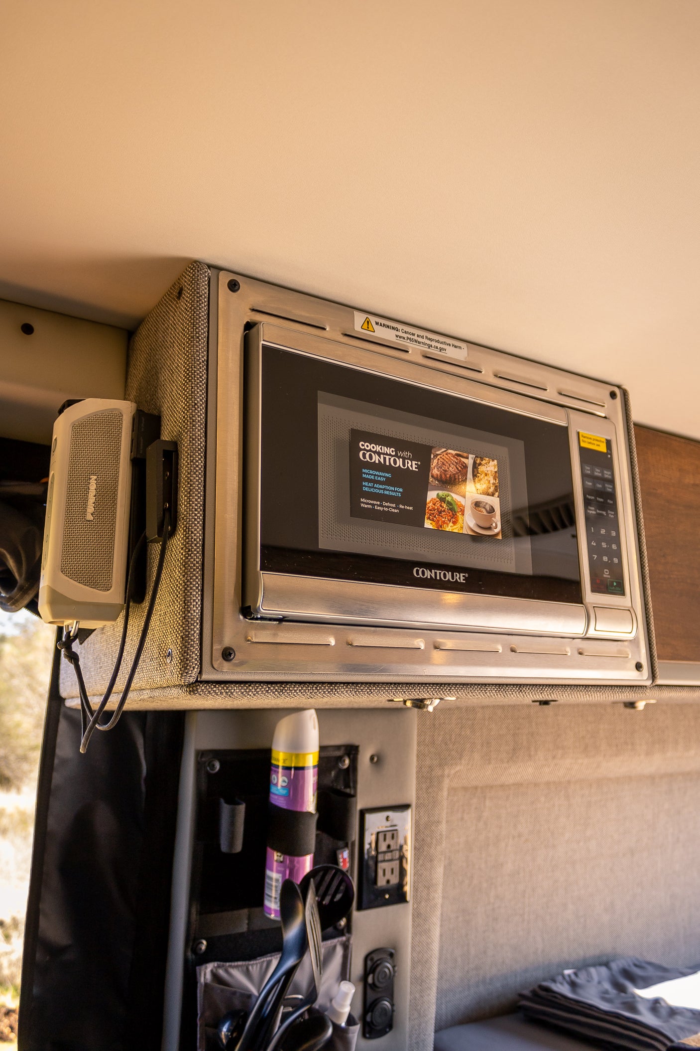 Compact RV rental kitchen featuring a mounted microwave, speaker, and organized storage for on-the-go meals.
