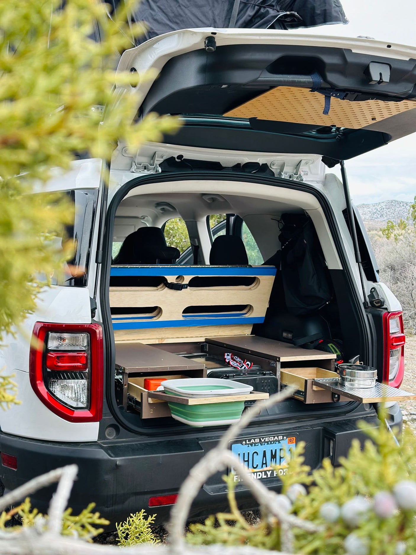 featuring a rooftop tent & rear camp kitchen. Desert scene with person relaxing under awning.|This custom car camping SUV