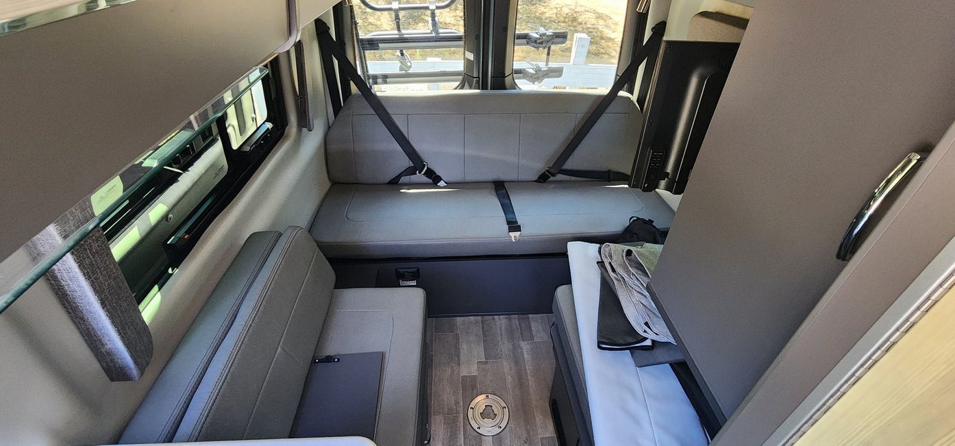 RV rental interior: Camper van with front dinette, rear bench seating/bed, TV, and wood-patterned floor.