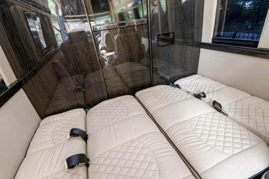 RV rental comfort: interior features plush, quilted seating that converts to beds, glossy wood accents, & window views.