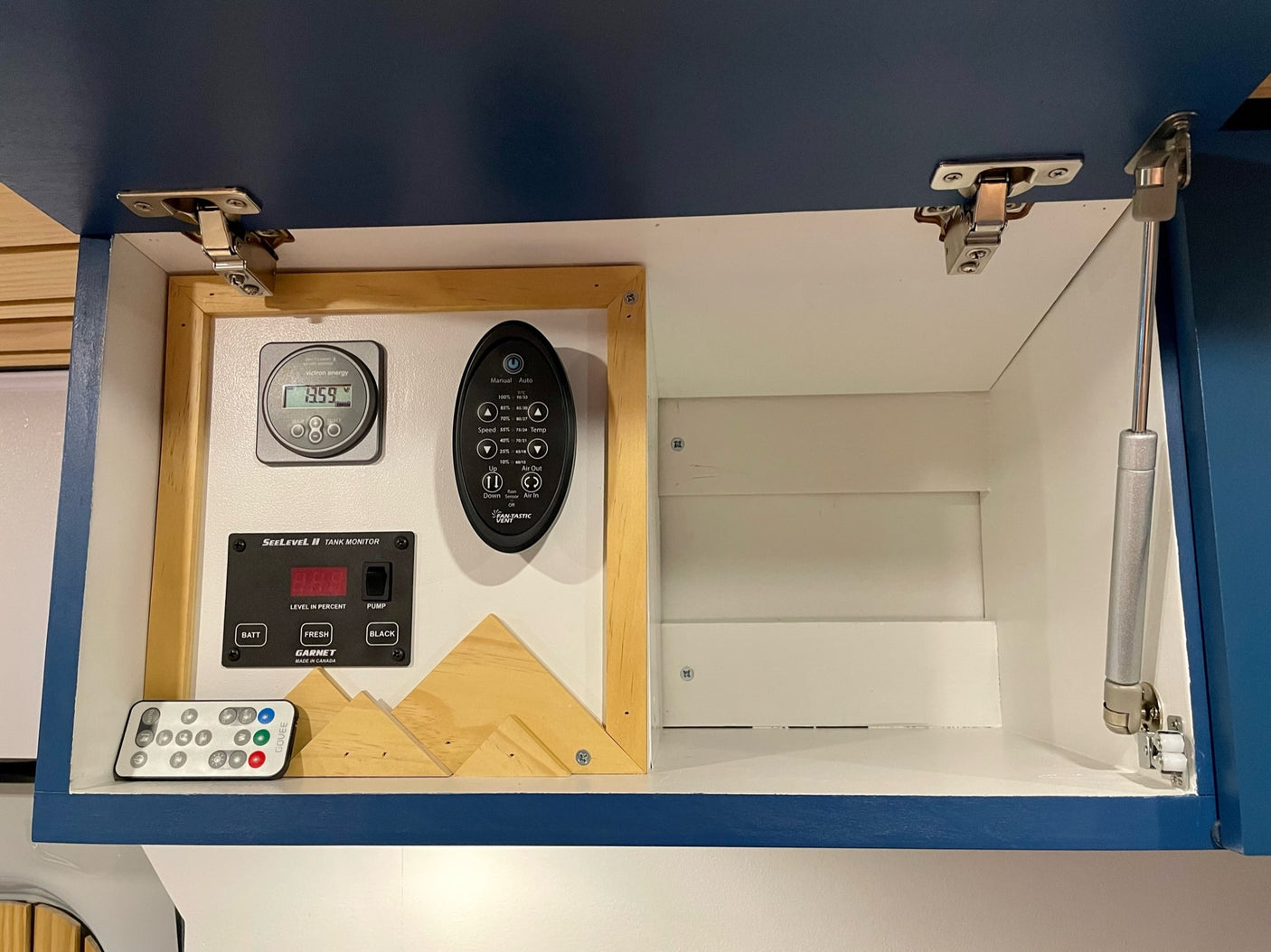 RV rental interior showing system controls: Victron energy monitor, tank levels, and fan remote in an open cabinet.