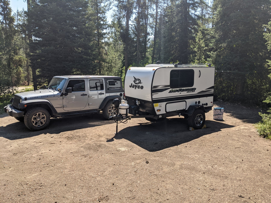 Jeep pulling a Jayco Jay Feather Micro RV camper at a sunny forest campsite. Great rv rental for adventure.|An RV rental trailer and Jeep at a campsite. Enjoying outdoor cooking from the Jay Feather Micro's rear galley.|Organized RV rental rear compartment features an outdoor kitchen with a Blackstone griddle