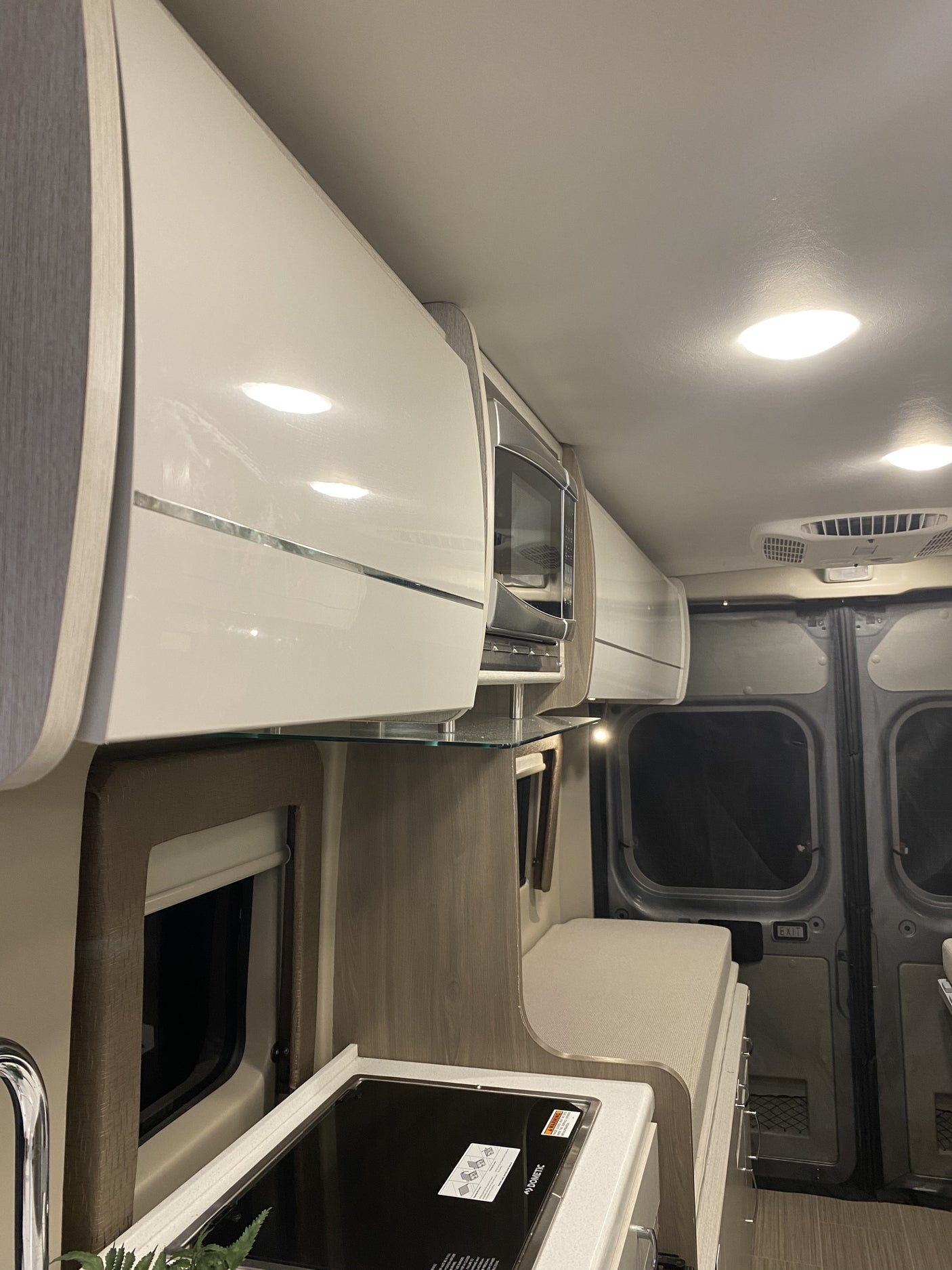 Modern RV rental interior: kitchen with Dometic stovetop, microwave, shiny overhead cabinets, and cushioned seating for comfy travel.