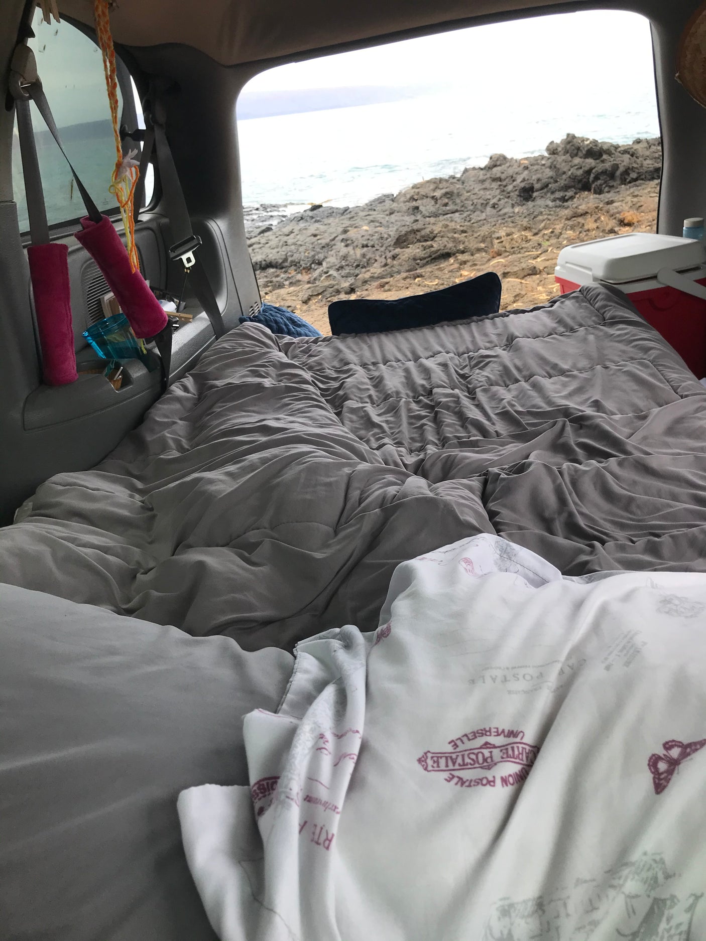 Inside a customized rv rental: a cozy bed with blankets and pillows, overlooking a rugged ocean coastline. Perfect for van life camping.