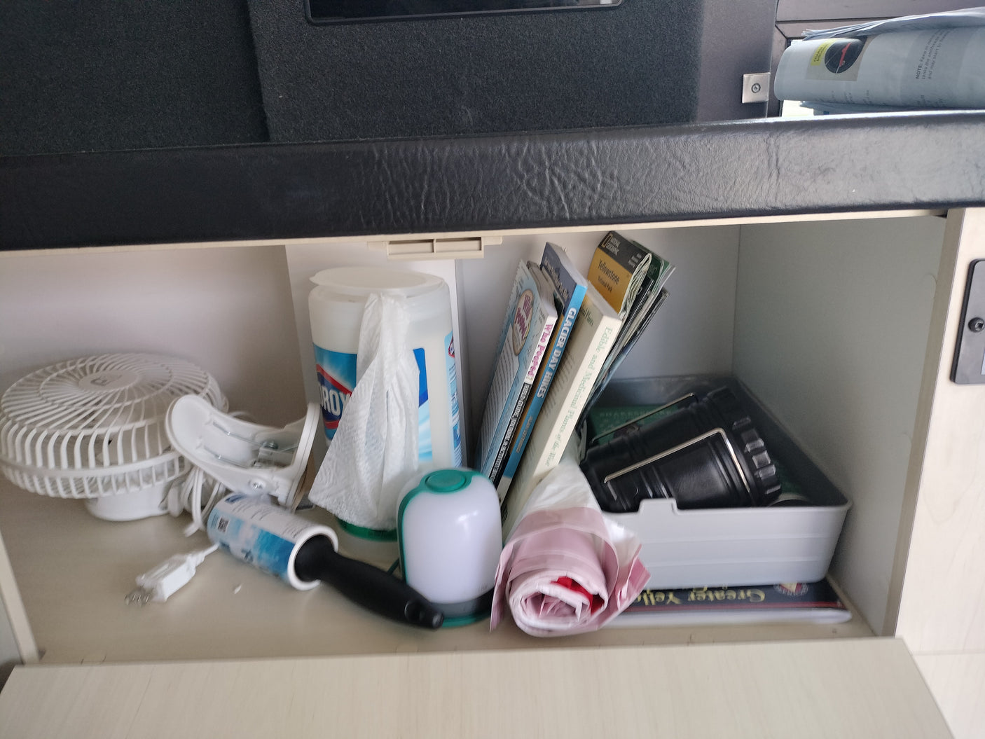 An RV rental's well-organized cabinet filled with a fan, cleaning supplies, and travel guides.