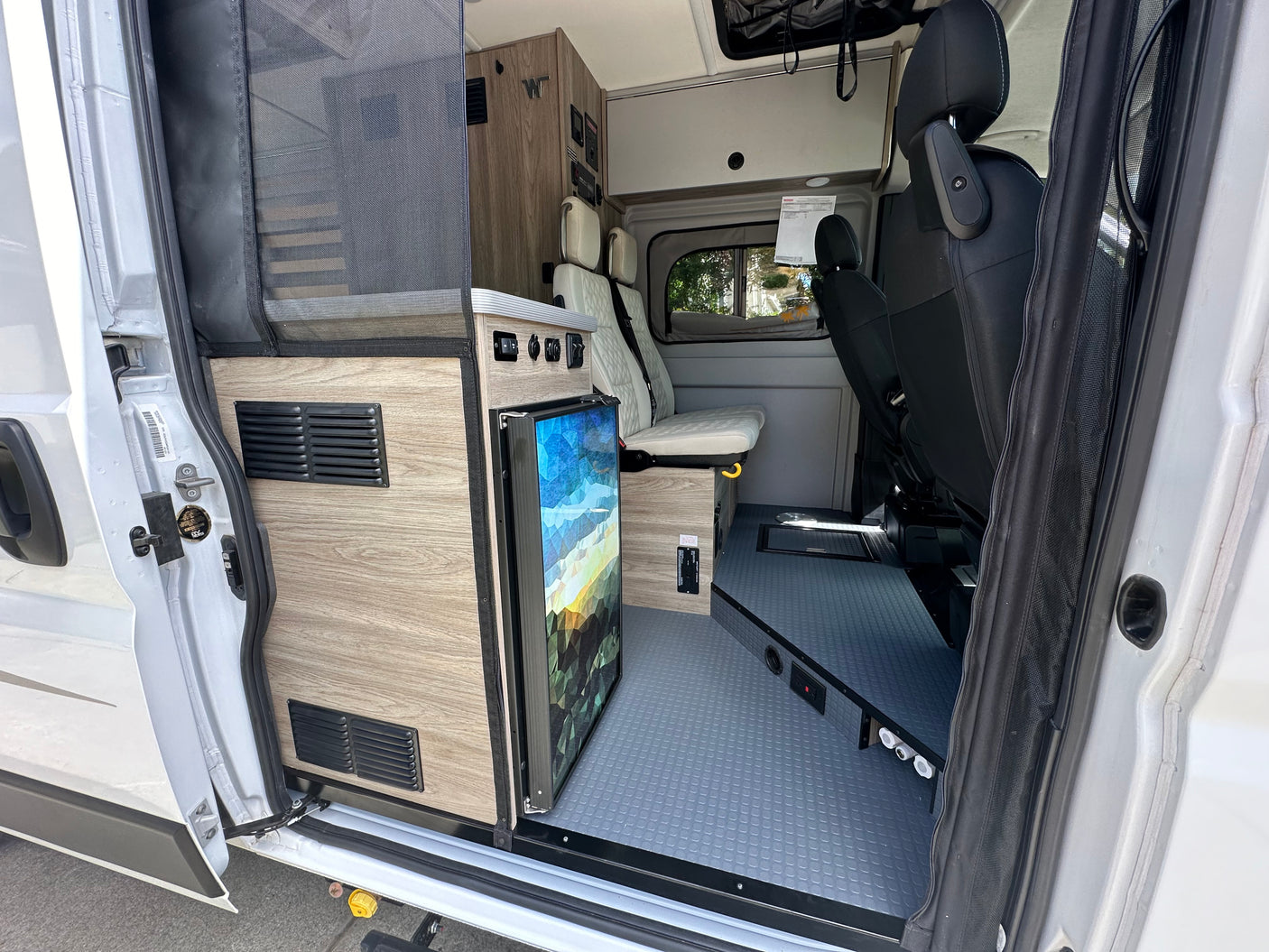 Compact RV rental interior featuring a fridge, adaptable seating, and wood finishes, ready for your next adventure.