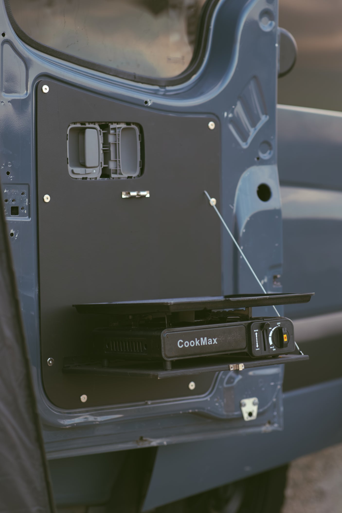 RV rental feature: A CookMax portable gas stove resting on a flip-down table mounted inside a van door, ready for camping meals.