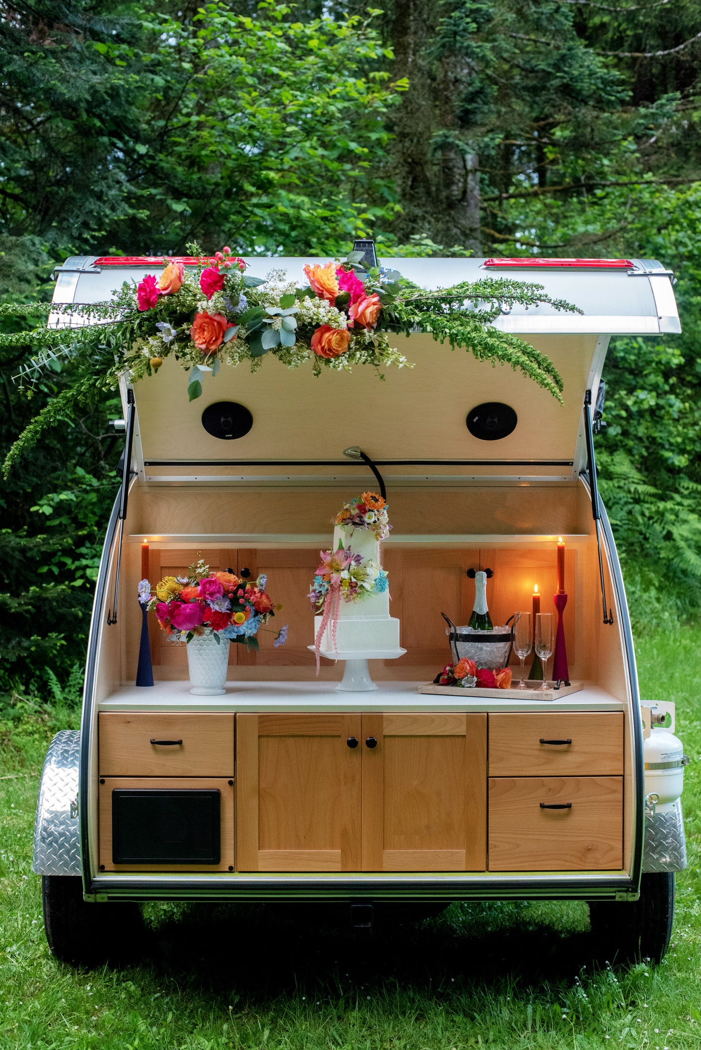 Charming teardrop camper RV rental setup with flowers, cake, and champagne, perfect for outdoor celebrations.