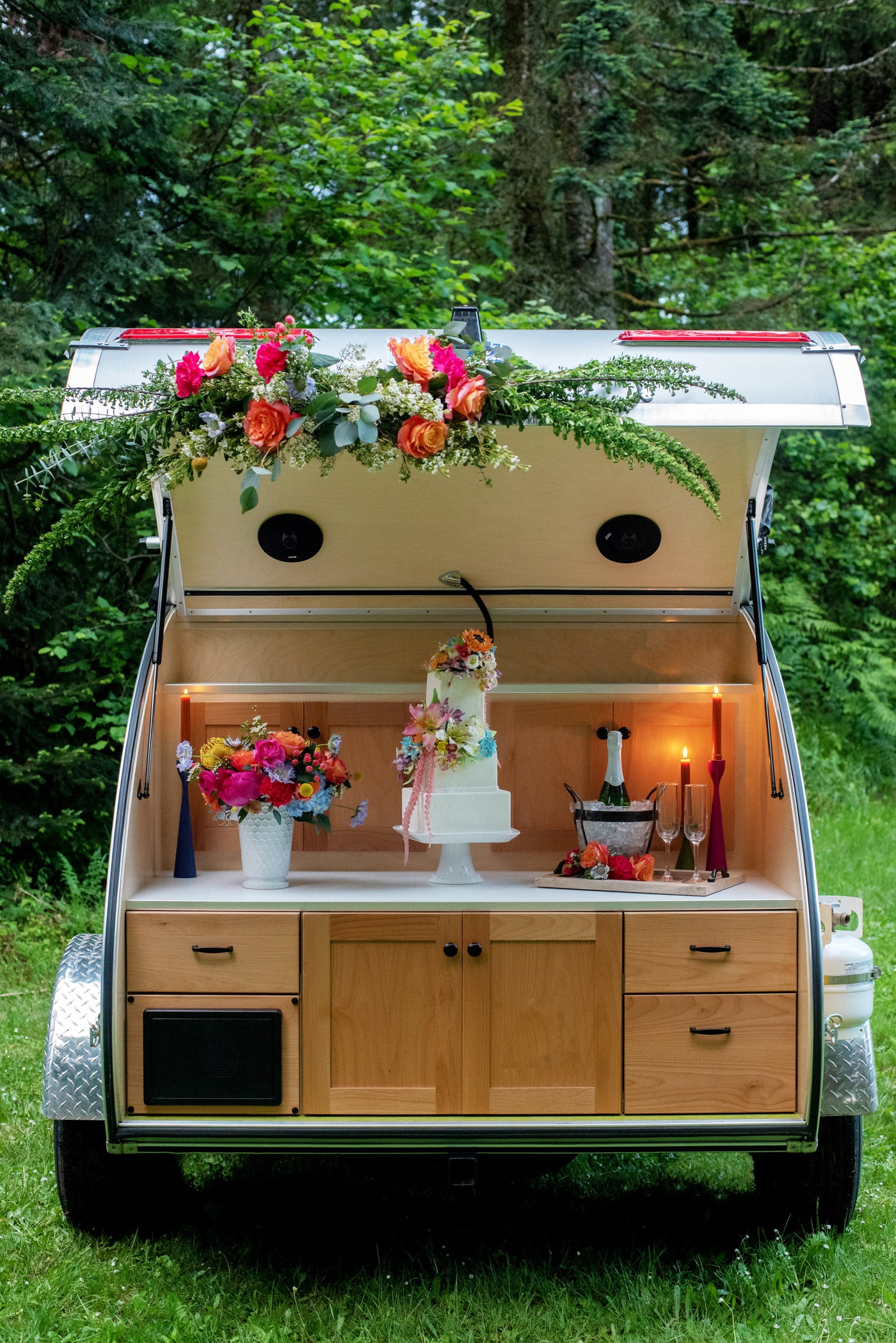 Charming teardrop camper RV rental setup with flowers, cake, and champagne, perfect for outdoor celebrations.