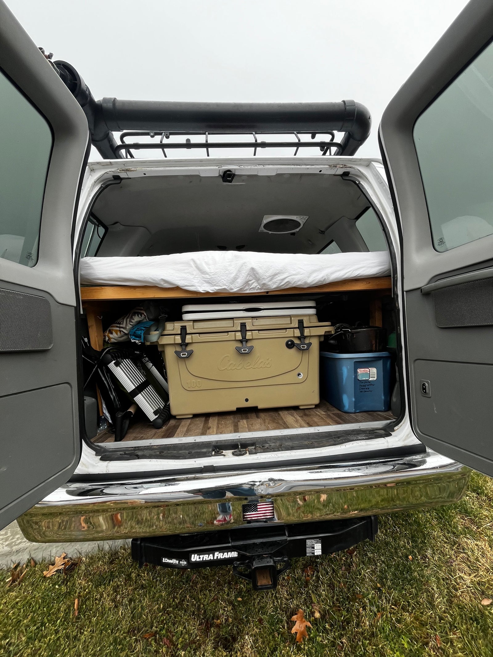RV rental van's organized back: bed, cooler, camping gear, roof rack, & hitch visible. Ready for adventure.