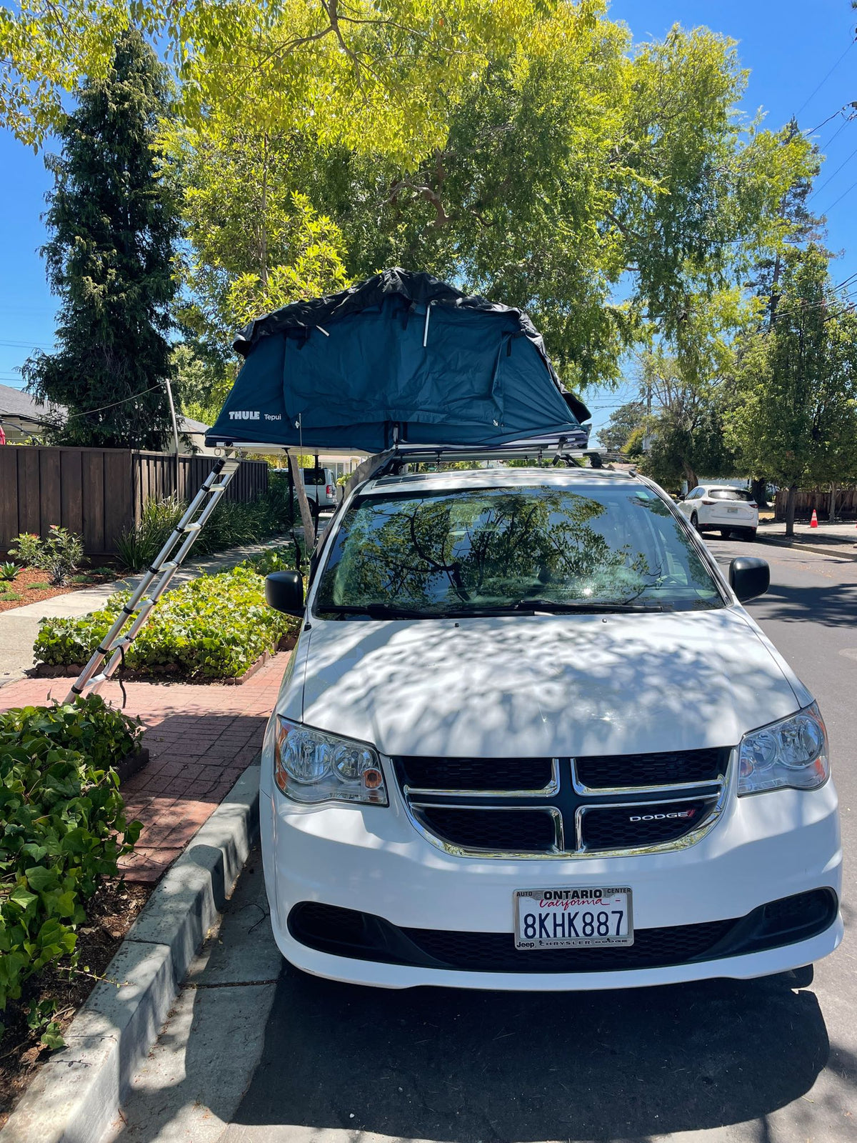 visible through the open side door of the white van.|A person attaches a black Yakima cargo carrier to a white RV rental vehicle