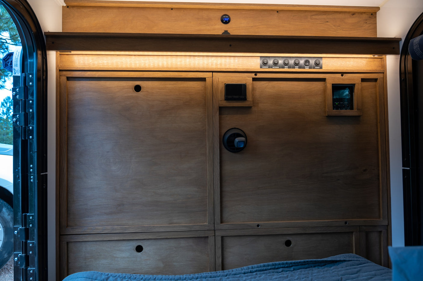 RV rental interior: wooden panels, power controls, thermostat, and bed, providing comfort and functionality.