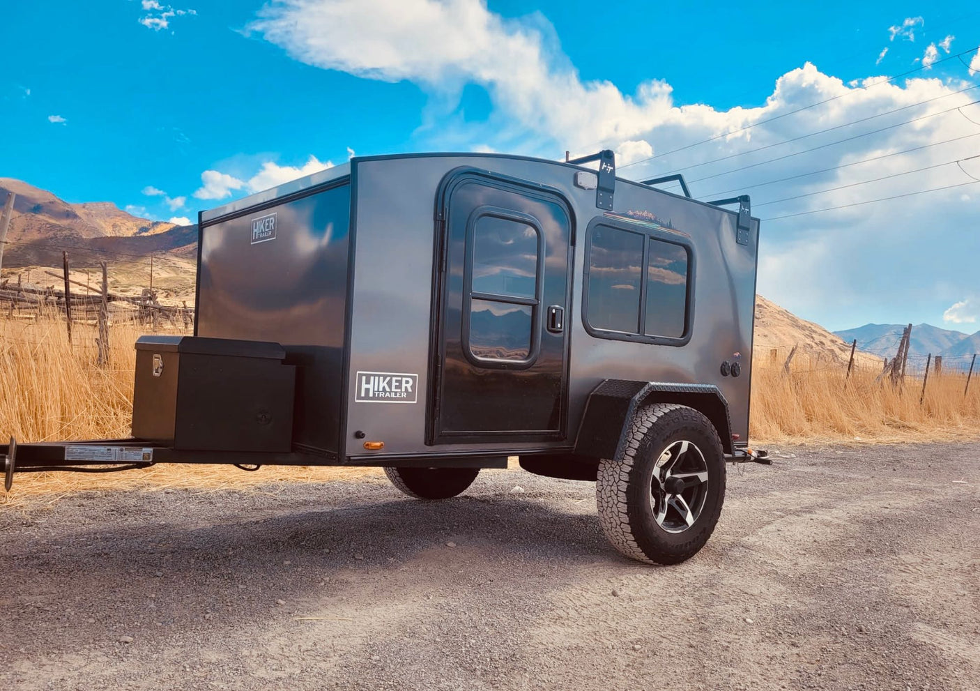 Adventure-ready Hiker Trailer RV rental parked on a scenic gravel road, mountains in background. Your perfect escape!