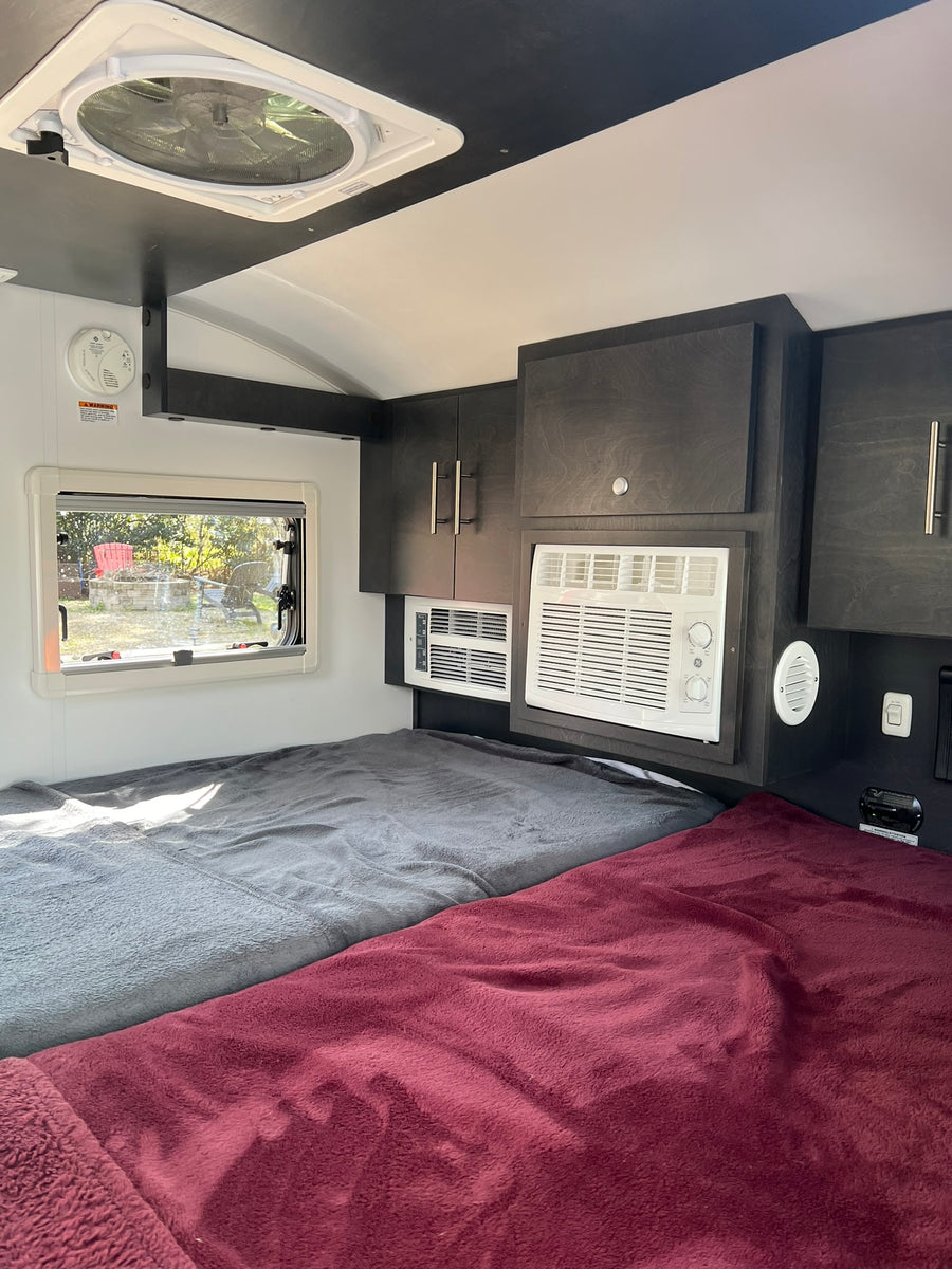 treed campsite.|White RV roof with two skylights and a black Yakima roof rack. Great for your next rv rental adventure!|Front view of a white teardrop travel trailer on gravel