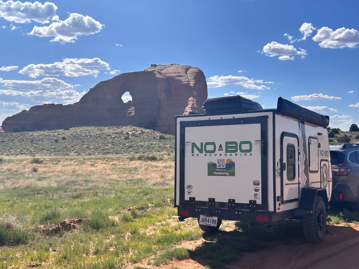 RV rental: A "No Boundaries" camper trailer, branded Outdoorsy, overlooks a massive natural arch in a sunny Wyoming landscape. — photo 2
