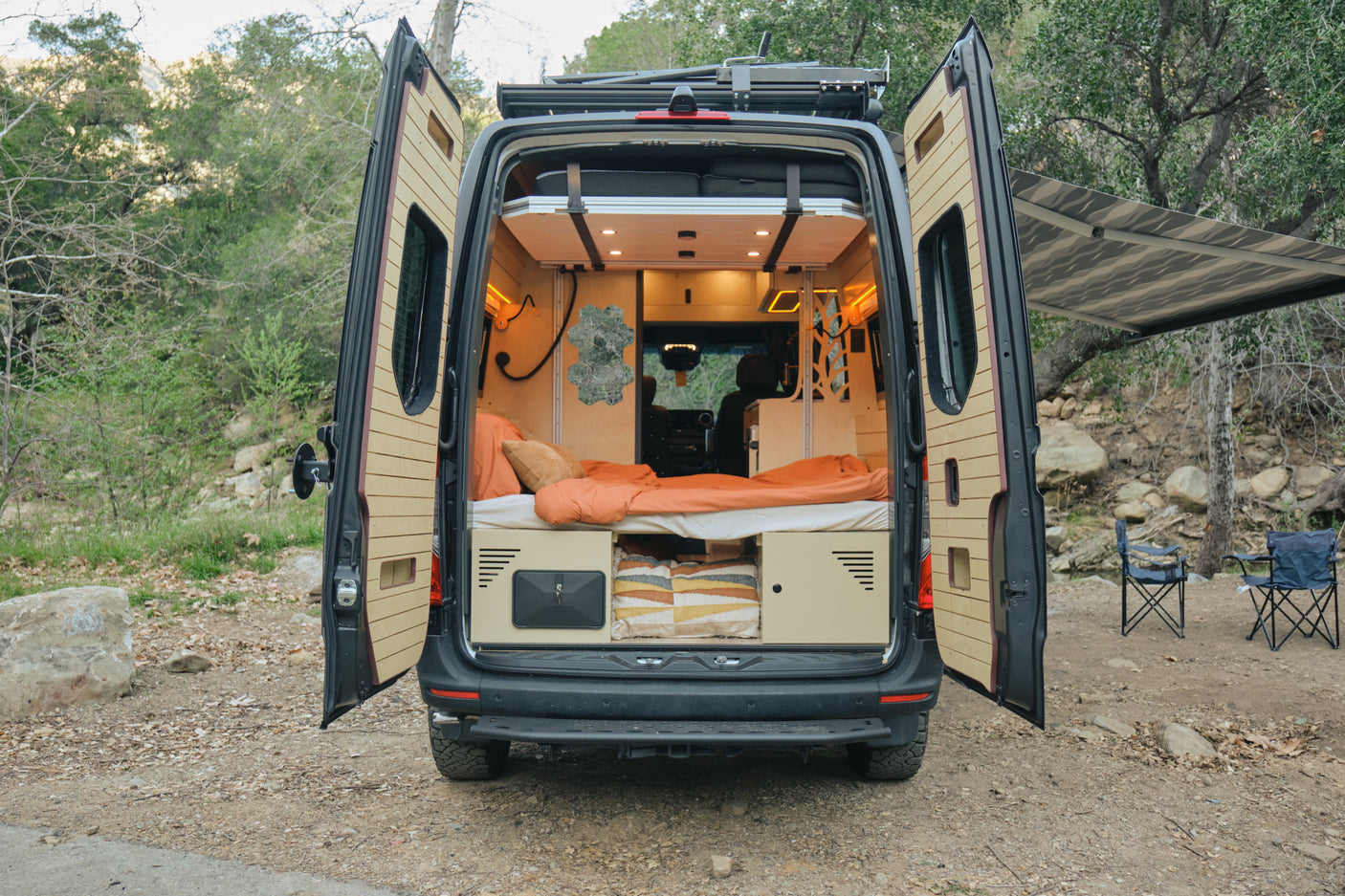 RV rental camper van with open doors, showing its cozy interior, bed, and outdoor setup with an awning and chairs.