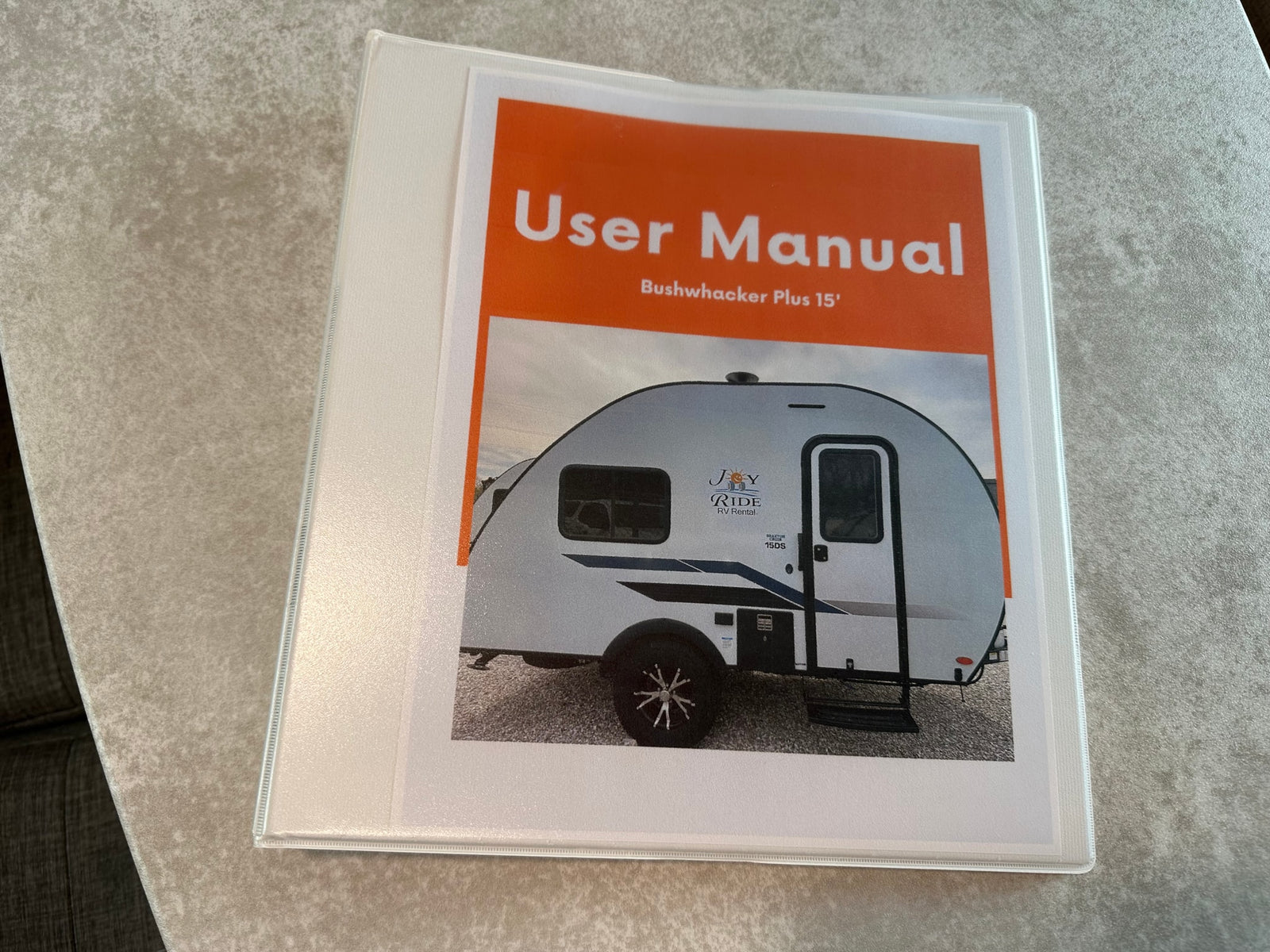 User Manual for a Bushwhacker Plus 15' travel trailer from Joy Ride RV Rental, presented in a white binder.