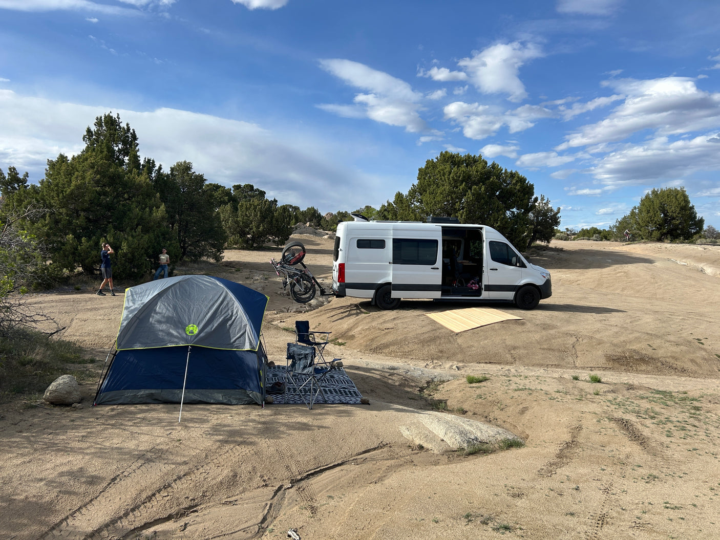 RV rental adventure: People, camper van, tent, and bikes at a scenic desert camp.