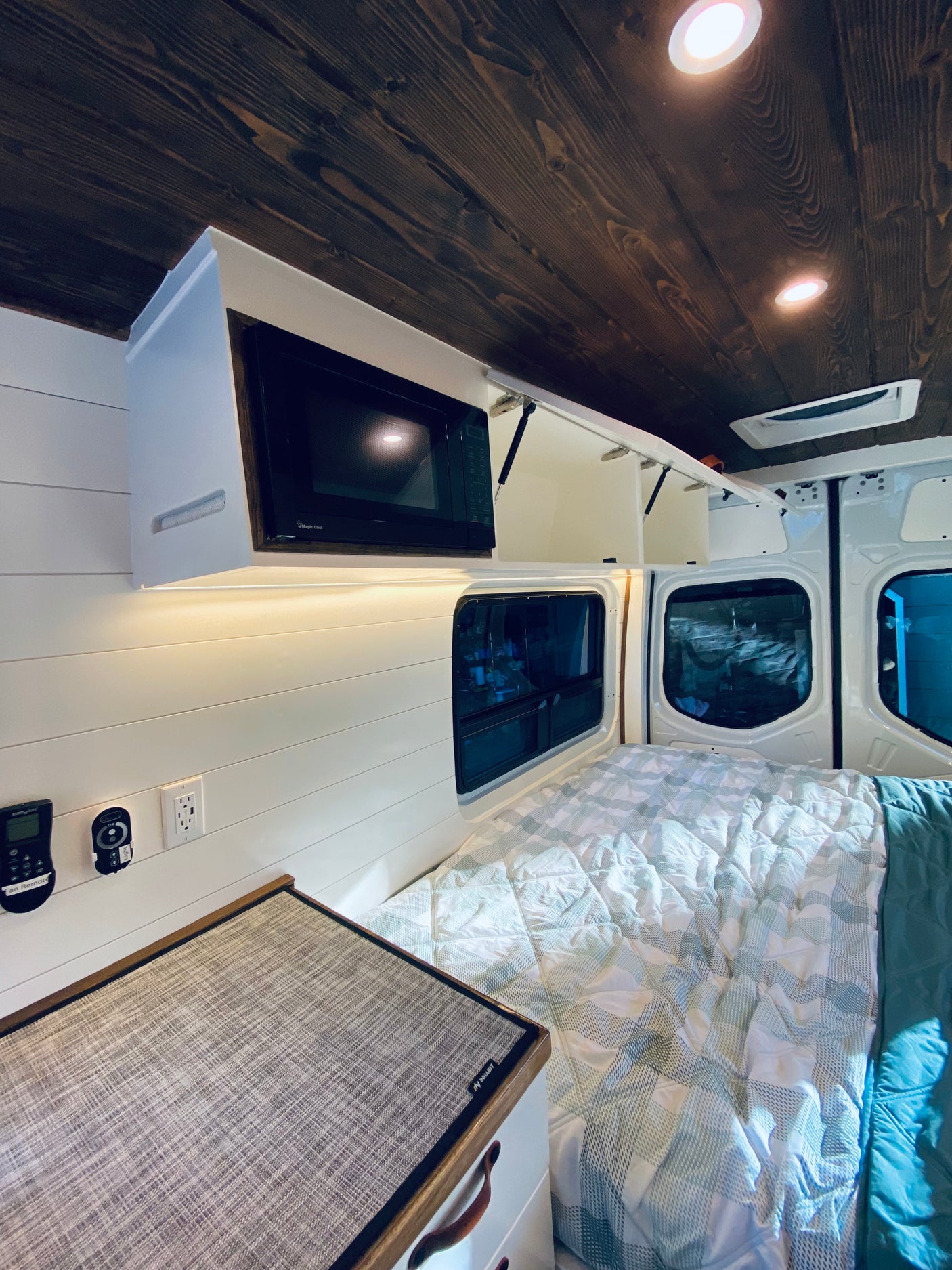 RV rental van conversion: a cozy interior with a microwave, custom wood ceiling, and comfortable bed.