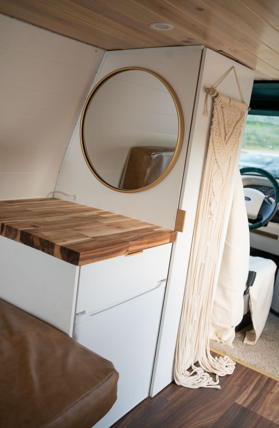 Stylish RV rental interior featuring a butcher-block counter, round mirror, and leather seating in a compact van.