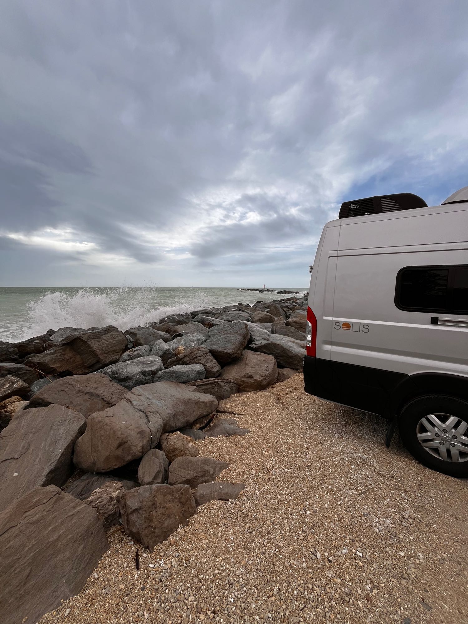 featuring a green Onan generator (OG 2800i) and mud dauber nests on the chassis.|Adventure awaits! This rv rental is parked by crashing waves & rocks on a cloudy beach. Perfect for coastal travel.