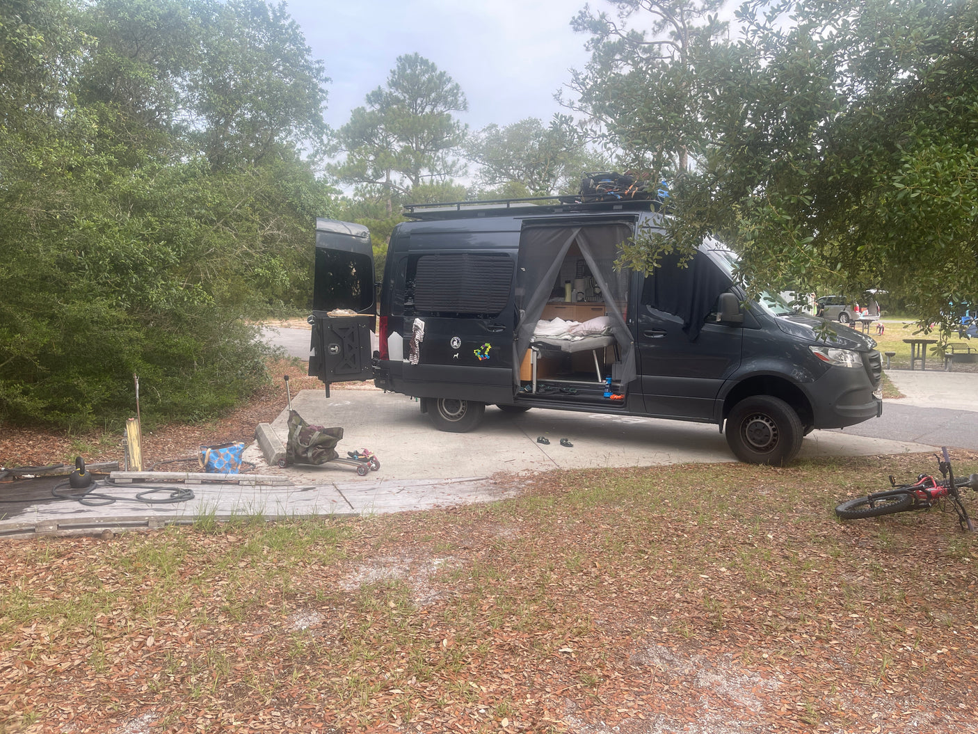 Spacious Mercedes Sprinter camper van at a wooded campground. Experience van life with this cozy RV rental.