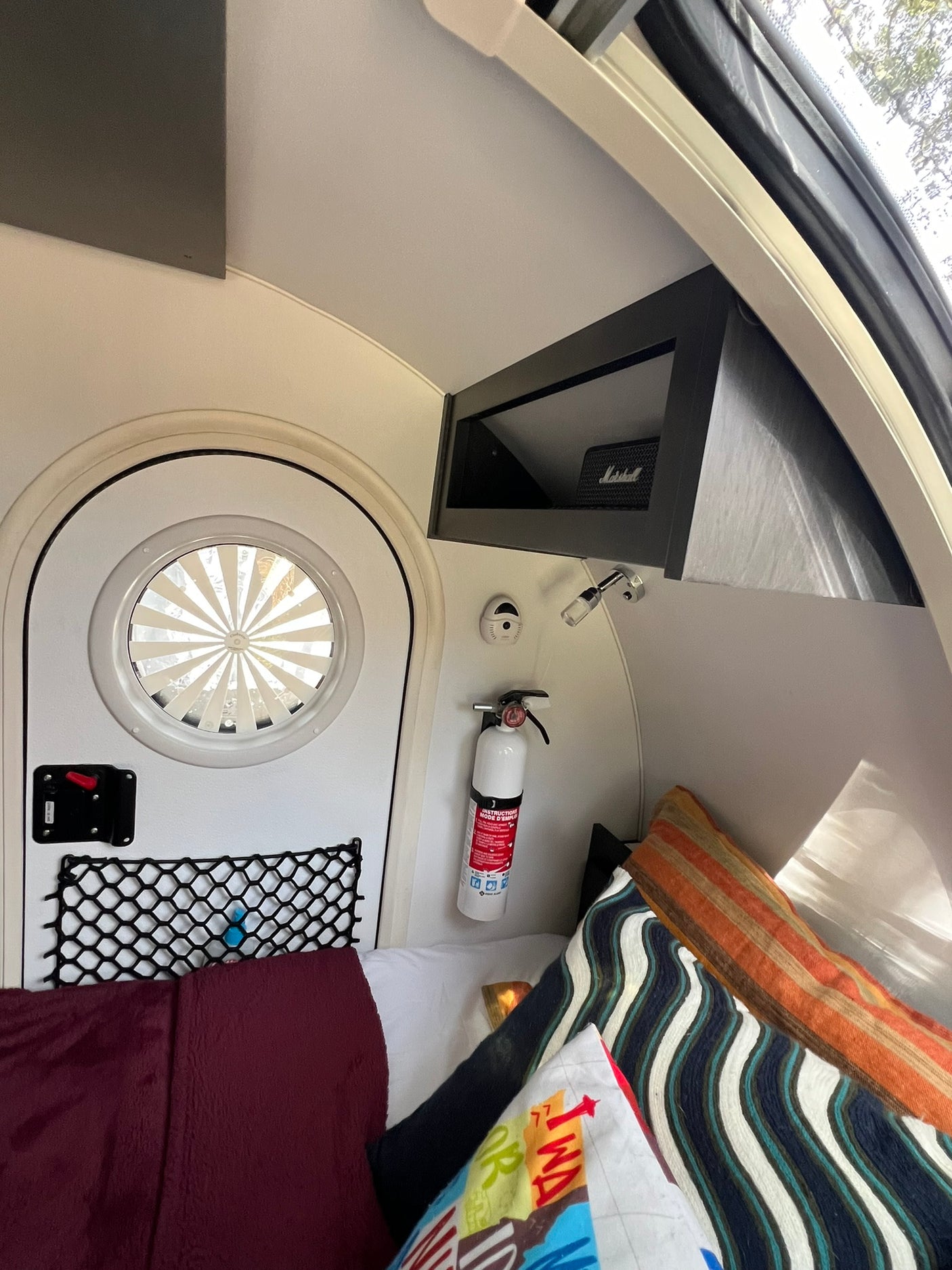 Compact RV rental interior: bed, round door, fire extinguisher, & storage net, perfect for cozy adventures.