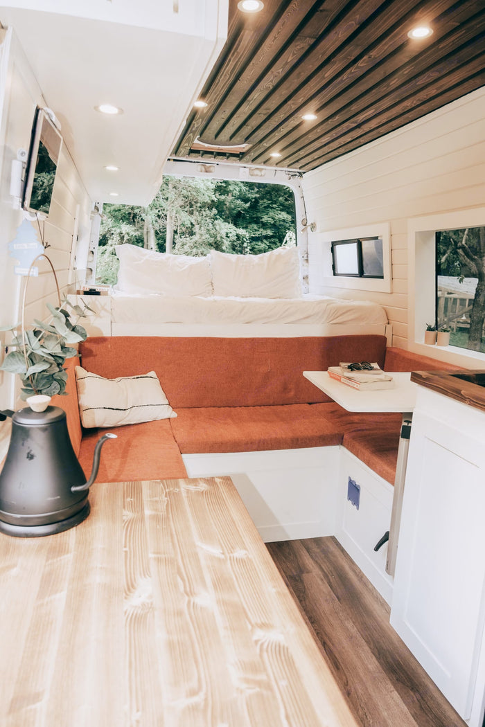 Inside a spacious RV rental: a comfy bed, L-shaped couch, dining table, & wood features. Ideal for travel.