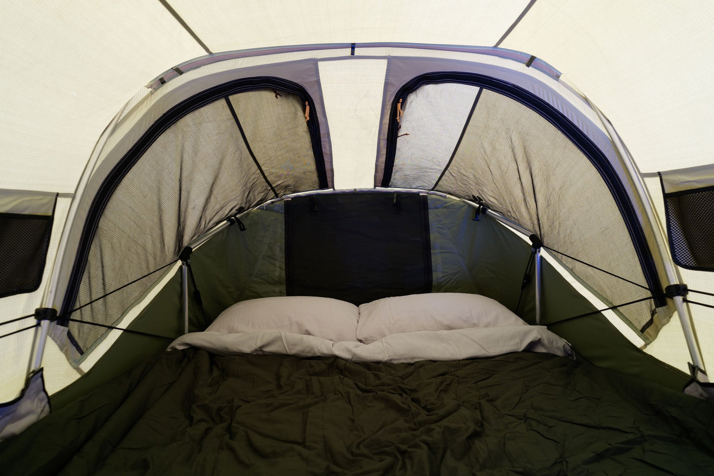 View inside an RV rental's built-in sleeping tent with a comfortable bed, pillows, and mesh openings for ventilation.
