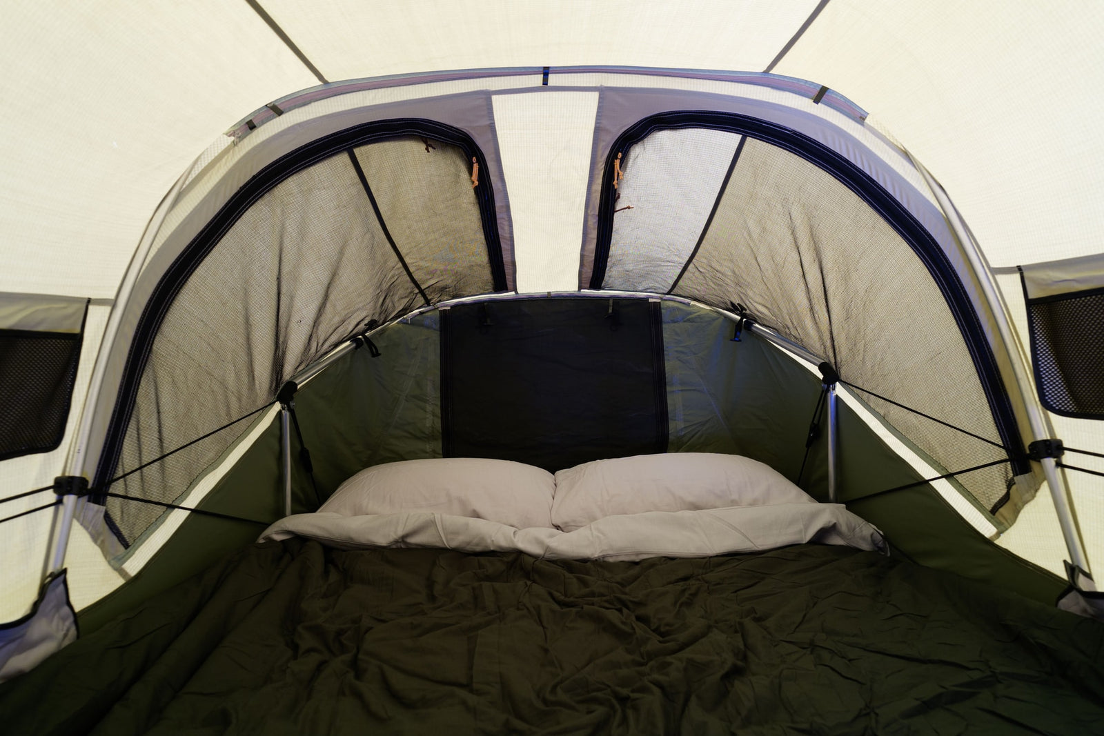View inside an RV rental's built-in sleeping tent with a comfortable bed, pillows, and mesh openings for ventilation.