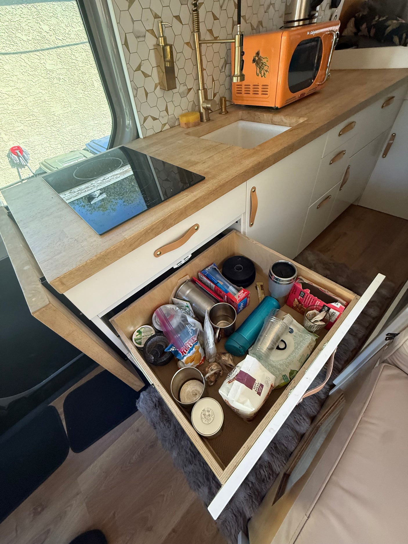 RV rental kitchen features wood counters, induction cooktop, sink, microwave, and an open drawer organized with supplies.