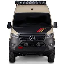 Front view: A tan & black Mercedes Sprinter adventure van, perfect for RV rental. Features off-road tires, bull bar & rooftop lights.