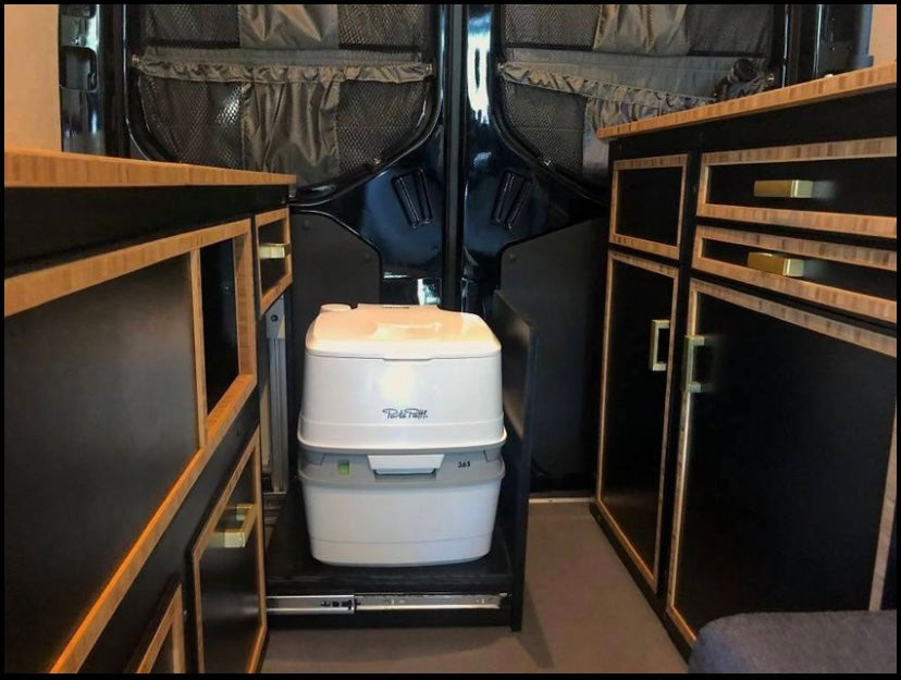 RV rental: Portable toilet stored on pull-out slide between custom black and wood cabinets, optimizing interior.