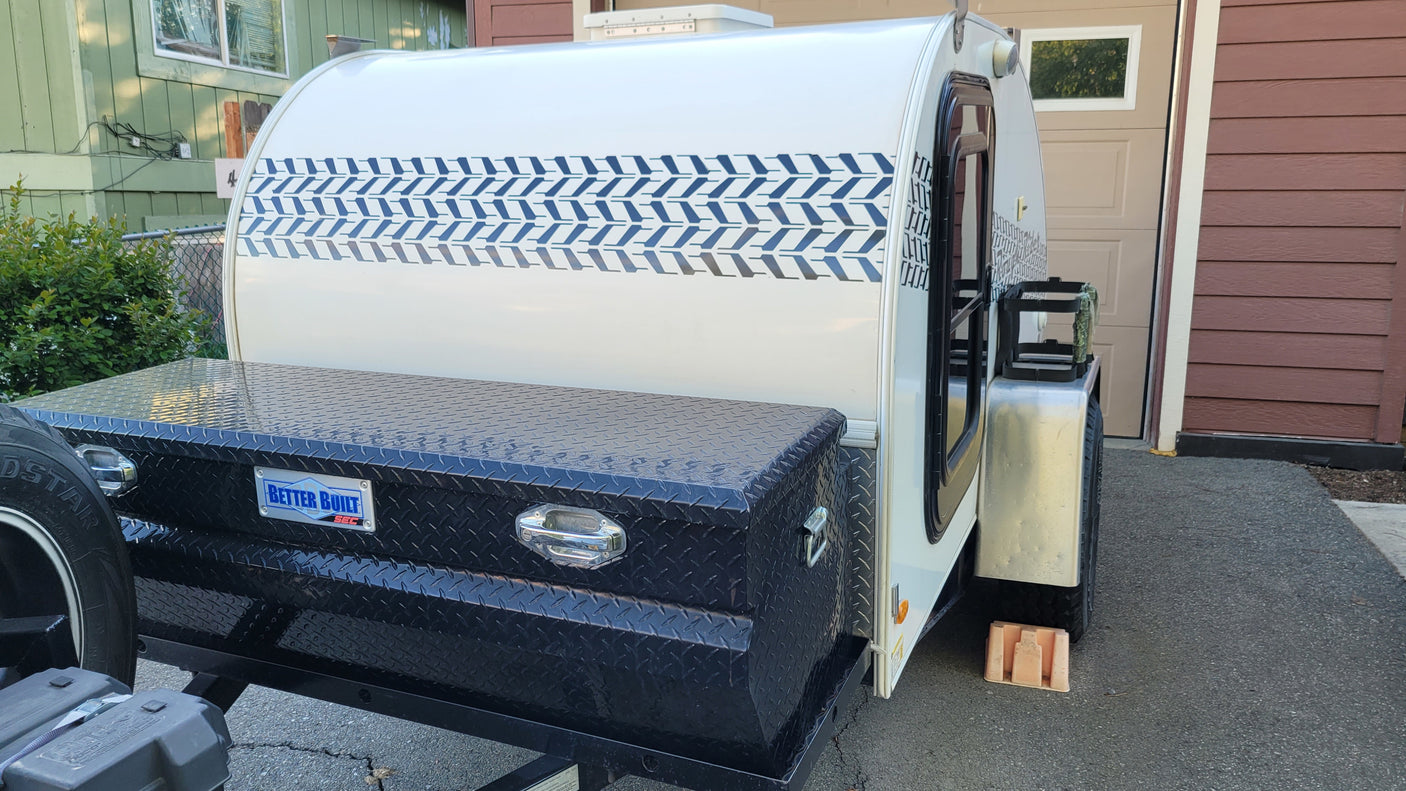 This white teardrop rv rental travel trailer, featuring a unique blue chevron pattern and front storage box, is ready for adventure.