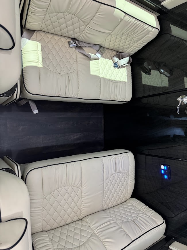 View inside a premium RV rental, featuring luxurious cream quilted seating, dark wood-look flooring, and sleek interior design. — photo 12