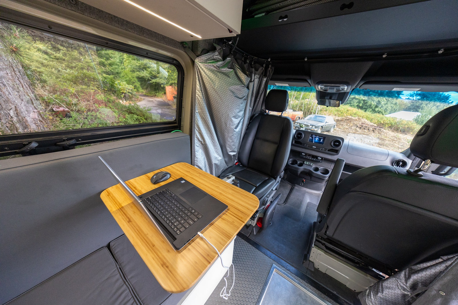 RV rental interior features a functional mobile office with a laptop, comfy bench, window view, and shower area.
