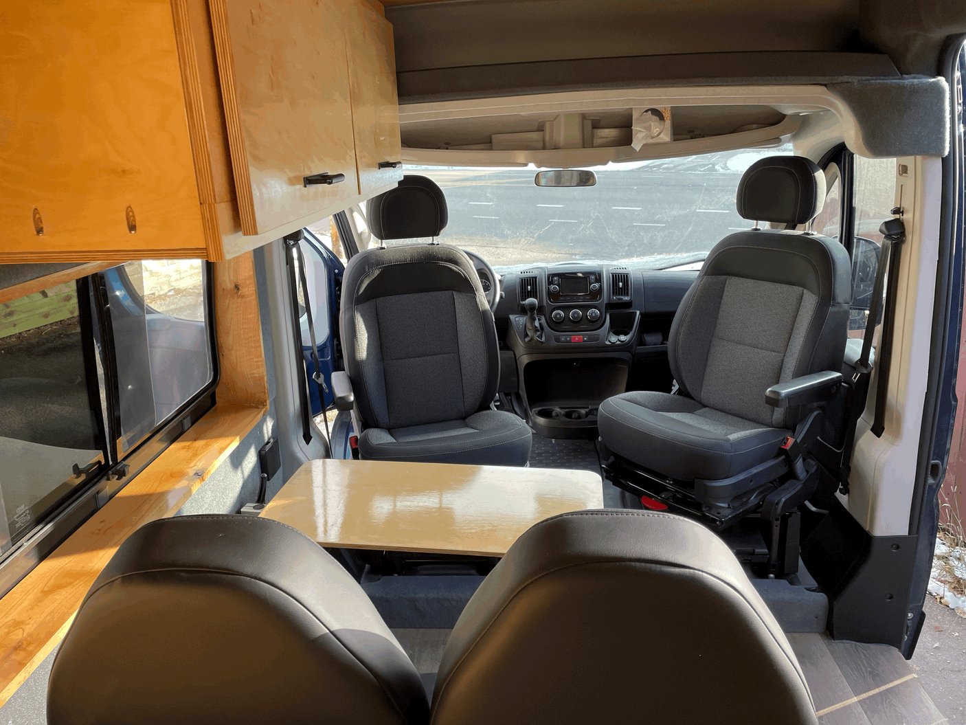 Inside this **rv rental** camper van: front swivel seats, a dining table, and wooden overhead storage for your journey.