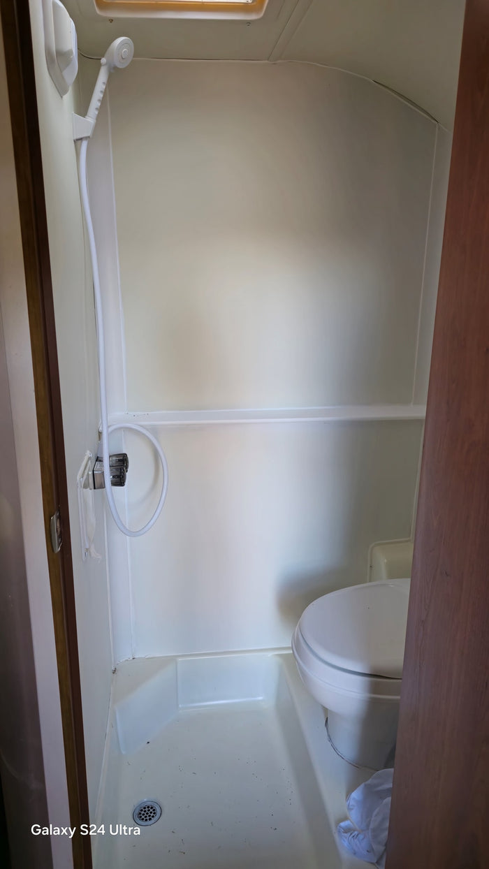 Step inside this RV rental's compact wet bath featuring a shower, toilet, and overhead skylight.